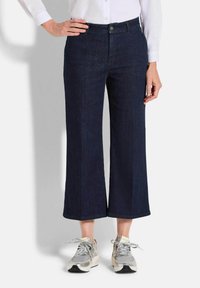 Culottes en denim bleu foncé avec une coupe large, dotées d'une fermeture à bouton sur le devant et de détails de couture subtils. Associées à des baskets grises.
