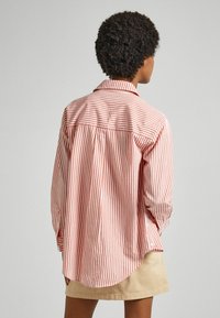 Camicia a maniche lunghe a righe rosse e bianche, con orlo curvo e polsini a bottoni. Realizzata in tessuto leggero, presenta un colletto classico.