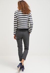 Pruhovaná krátká bunda v námořnické modré a krémové barvě, doplněná šedými přiléhavými kalhotami. Modelka má na sobě námořnicky modré semišové boty na vysokém podpatku. Zobrazen pohled zezadu.