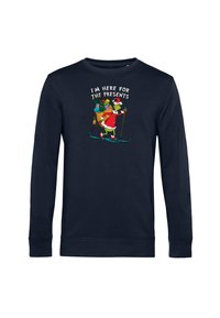 Felpa blu navy con maniche lunghe, che presenta un personaggio dei cartoni animati in un vestito da Babbo Natale, mentre scia con dei regali; il testo recita "SONO QUI PER I REGALI."