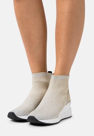 Botas de stretch metálicas doradas hasta el tobillo con acabado texturizado, que presentan una suela blanca y una suela exterior negra de goma. Acentos en azul claro en la parte superior.