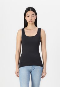 Schwarzes, figurbetontes Tanktop mit quadratischem Ausschnitt und breiten Trägern, aus glattem Stoff. Kombiniert mit hellblauen, eng anliegenden Jeans.
