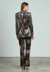 Traje con estampado de piel de serpiente metálica en tonos dorado, bronce y negro, que incluye un blazer entallado y pantalones ajustados, de textura suave.