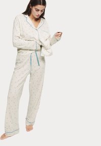 Set di pigiama in cotone color crema con dettagli blu. Caratterizzato da una camicia con bottoni, maniche lunghe e pantaloni larghi con un motivo discreto.