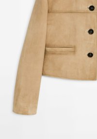 Beige suède jack met een cropped ontwerp, voorzien van een platte kraag, vier zwarte knopen en een zijzak. Soepele textuur.