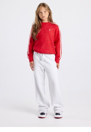 Suéter rojo de punto con rayas blancas en las mangas, combinado con pantalones deportivos gris claro. Zapatillas negras y blancas completan el conjunto.