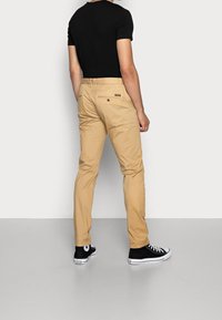 Khaki bukser lavet af bomuldsblanding, med en slim fit, baglomme med knap og parret med sorte høj-top sneakers.