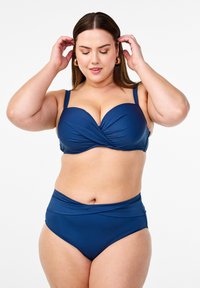 Námornícky modrý bikini s prekrúteným dizajnom na vrchnej časti, nastaviteľnými ramienkami a vysokým pásom so zberaním látky. Hladká textúra.