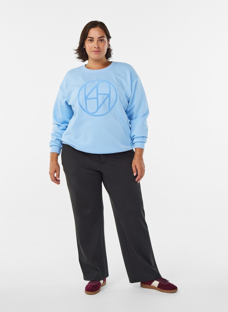 Light blue sweatshirt with round neckline and logo design on front, paired with black trousers and burgundy sneakers. Smooth texture.