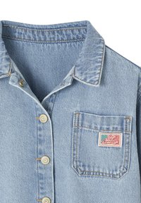 Light blue denim shirt with metallic buttons and a chest pocket featuring a small colorful patch with text.