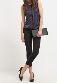 Satin navy blouse with a tie detail, paired with black fitted trousers and black stiletto heels. Holding a black clutch bag.