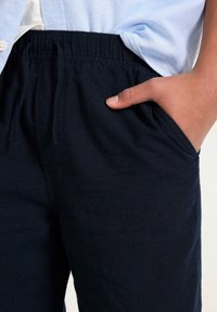 Granatowe bawełniane spodnie z elastycznym pasem, kieszeniami bocznymi i gładką fakturą. Szczegół ręki opierającej się w kieszeni, styl casual.