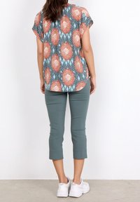 Mønstret kortærmet top med multicolor blomster på en blå baggrund; parret med lysegrønne, cropped bukser og hvide sneakers.