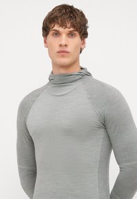 Haut ajusté à manches longues en tissu ribbé gris clair. Il présente un col structuré haut et une surface texturée avec un motif de grille subtil.