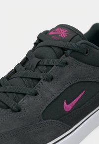 Nike SB kedai tamsiai tamsiai pilka žydra bei audinys. Yra rožiniai logotipo akcentai, tekstiliniai raišteliai ir balta guminė podinė.