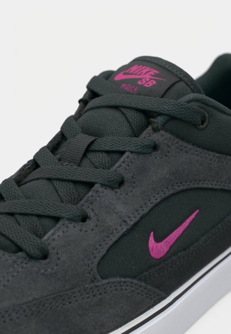 Zapatilla Nike SB en ante y tela gris oscuro. Presenta detalles del logotipo en rosa, cordones textiles y una suela de goma blanca.