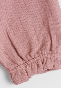 Tissu tricoté rose avec un motif texturé, doté d'un poignet élastique froncé en bas, créant un bord doux et légèrement froncé.