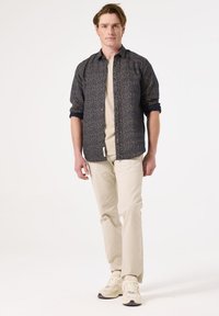 Camisa abotonada en azul marino con un patrón floral, combinada con una camiseta beige y pantalones crema. El modelo lleva zapatillas deportivas claras.