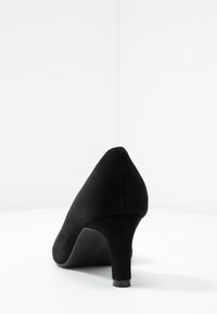 Chaussure noire en daim à talons hauts avec un bout pointu et un talon modéré, présentant une texture lisse et un design simple.