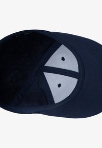 Olujna kapa s teksturiranim tkanjem, dizajnom sa šest panela i vezanim rupicama za ventilaciju. Unutrašnjost sadrži mekanu podstavu.