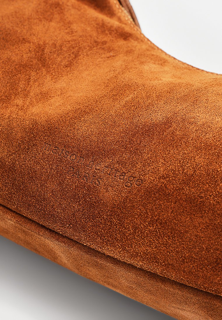 Braune Wildlederschuhe mit einer glatten Oberfläche, die über ein geprägtes Branding verfügen. Das Design ist einfach mit einer runden Zehenform und minimalen Akzenten.