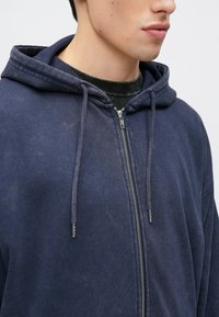 Navy blue zip-up hoodie with a soft texture, drawstrings, and a metal zipper. Features a large hood and casual fit.