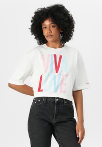 Balta trumpa marškinėliai su ryškiu raudonu, rožiniu ir mėlynu "VIVA LOVE" užrašu. Trumpomis rankovėmis. Derinama su aukštu juosmeniu juodomis džinsomis.