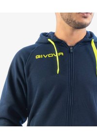 Felpa con zip di colore blu navy realizzata in tessuto morbido, dotata di tasca a marsupio e cordini gialli brillanti; logo "GIVOVA" ricamato sul petto.