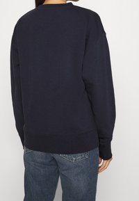 Pullover blu navy realizzato in tessuto morbido, caratterizzato da un collo rotondo, spalle scese e polsini a costine. Indossato con jeans azzurri.