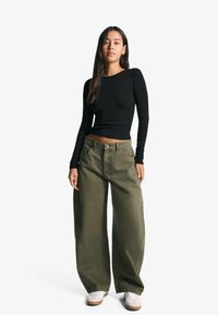 Black long-sleeve top paired with loose-fit, olive green wide-leg pants and white sneakers, highlighting a casual, relaxed style.