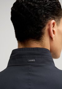 Schwarzer Jackenkragen mit einem Etikett auf der Rückseite, das "JOOP!" liest, mit einer glatten Textur und strukturiertem Design.