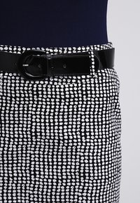 Svart och vit kjol med ett prickigt mönster, med ett glansigt svart bälte och en åtsittande design som framhäver en strukturerad form.