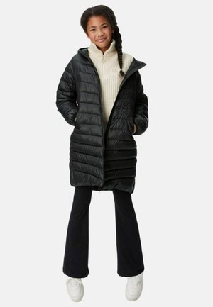 Giubbotto trapuntato nero con design a righe verticali, cappuccio e tasche laterali, indossato sopra un maglione crema a collo alto, abbinato a pantaloni neri a campana.
