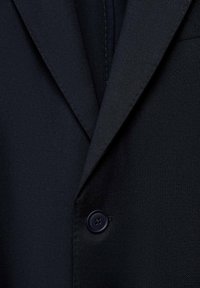 Granatowa marynarka z teksturowanej tkaniny, z klapami i jednym czarnym guzikiem z przodu.