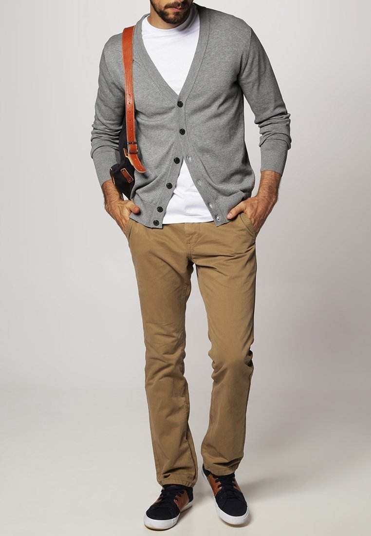 Homme portant un cardigan gris boutonné, un t-shirt blanc, un pantalon kaki et des baskets noires avec des accents marron, portant un sac en cuir marron à bandoulière.