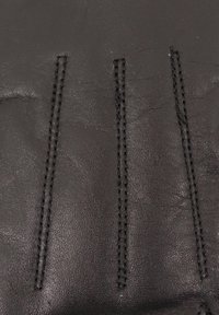 Schwarzes Leder mit einer glatten Textur, das drei markante genähte Linien aufweist. Die Oberfläche ist leicht glänzend und zeigt natürliche Falten.