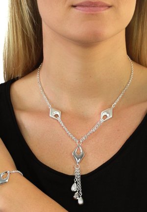 Silver necklace with a chain design featuring diamond-shaped accents and hanging teardrop elements, worn on a black shirt.