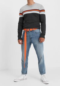 Pull rayé gris et noir avec accent orange, associé à un jean bleu clair, une ceinture orange et des baskets blanches. Convient pour une tenue décontractée.