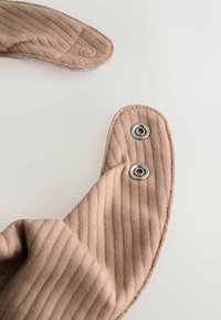 Tissu côtelé beige avec deux boutons-pression métalliques sur une sangle incurvée, sur un fond blanc uni.