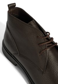 Bottines en cuir marron avec surface texturée, design à lacets, couture renforcée et semelle en caoutchouc plate. Accentué par une languette.