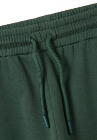Grüner Baumwoll-Jogginghosenbund mit strukturiertem Rippstrick, ausgestattet mit einem Kordelzug mit Kunststoffspitzen. Glattes Gewebe mit leicht gebürstetem Finish.