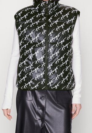 Schwarze gesteppte Weste mit weißem diagonalen "Hugo"-Schriftzug, getragen über einem weißen Langarmshirt und kombiniert mit einem schwarzen Lederrock mit Knöpfen.