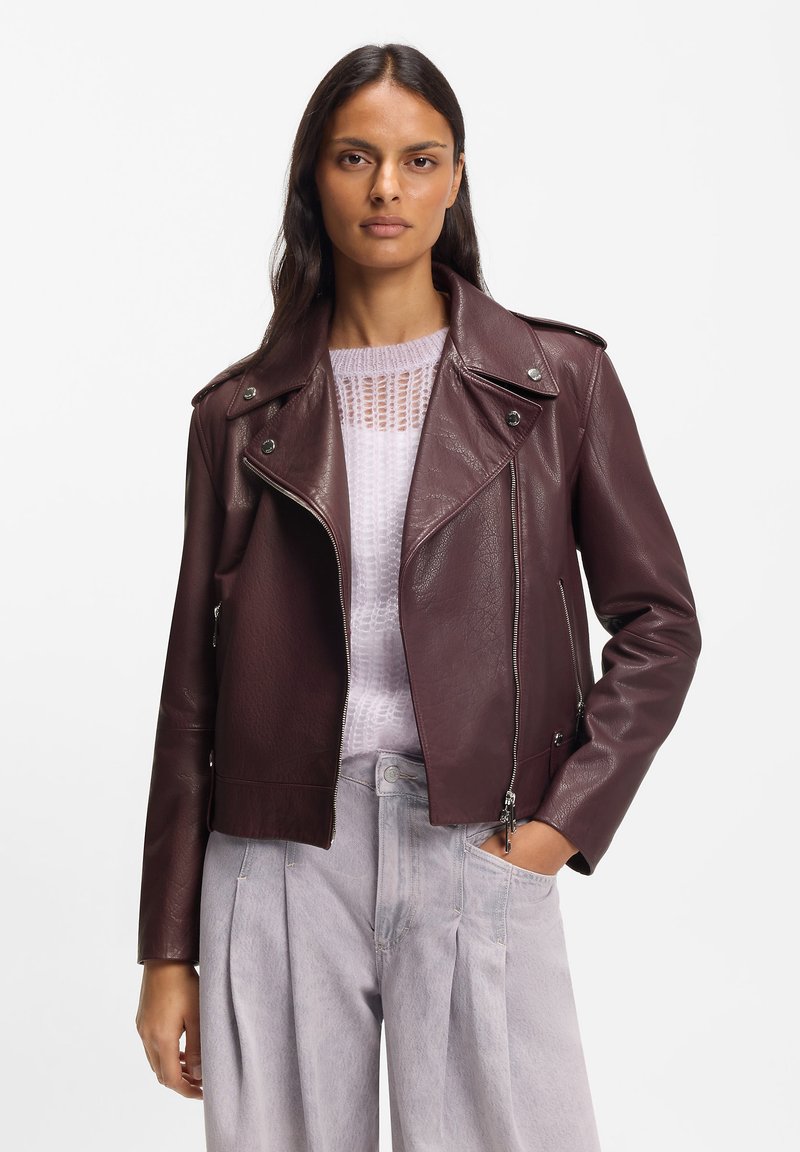 Burgundy leather biker jacket with silver-tone hardware, zip closure, and notched collar; worn over a light knit top and light gray pants.