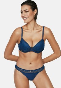 Marineblauw lingeriesetje met een kanten beha met voorgevormde cups en verstelbare bandjes, in combinatie met een bijpassende string met kanten afwerking.