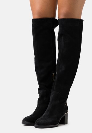 Schwarze Wildleder-Stiefel über dem Knie mit einem breiten Absatz, seitlichem Reißverschluss und minimalen Nähten. Glatte Textur und figurbetontes Design.