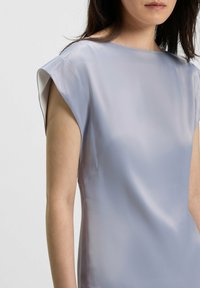 Blusa di un leggero lavanda con maniche a cappotto, texture satinata liscia e un sottile lucido. Presenta un collo a barca e una silhouette aderente.