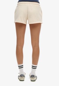 Shorts en polaire beige clair avec une taille élastique, des poches latérales et un ourlet au-dessus de la cuisse. Portés avec des chaussettes rayées à la cheville et des chaussures.