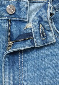 Tissu en denim bleu avec une fermeture éclair métallique ouverte, une boutonnière et un bouton argenté sur un jean.
