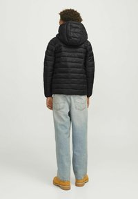 Zwarte pufferjack met horizontaal quiltpatroon en een capuchon. Combineert met lichtblauwe spijkerbroek en tan laarzen, met een ontspannen pasvorm.