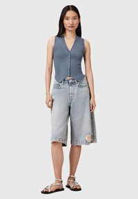 Blaues geripptes ärmelloses Oberteil mit V-Ausschnitt und Knopfverschluss, kombiniert mit hellen, ausgefransten Denim-Bermudashorts und silbernen Riemchensandalen.